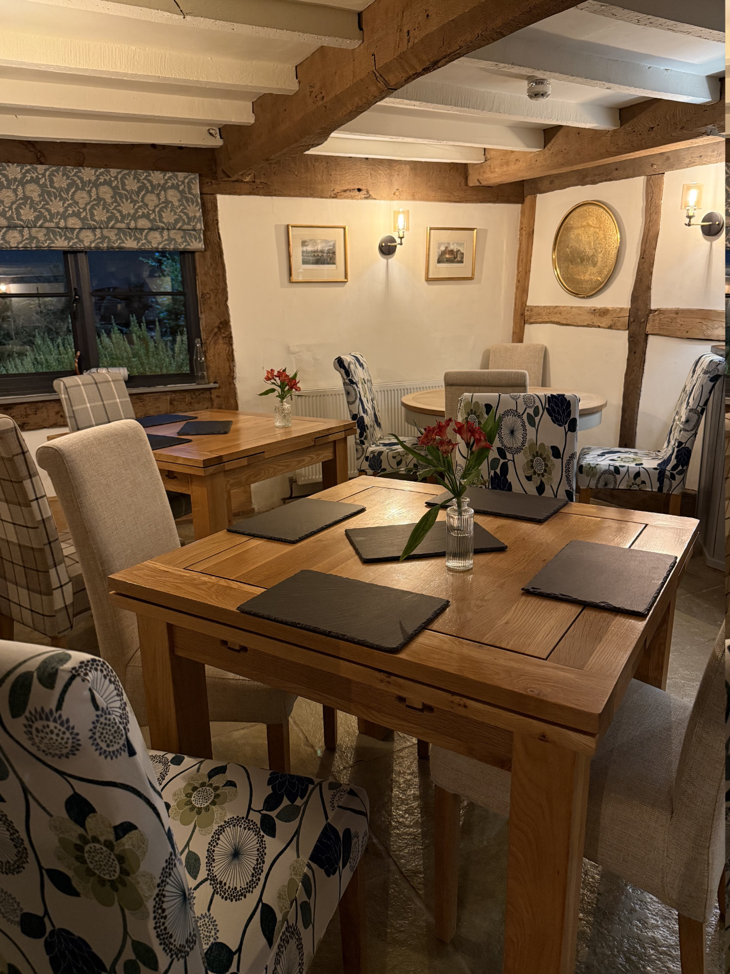 Oak tables laid with slate mats and fresh flowers beneath low timber beams